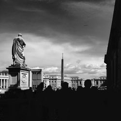 People walking in city against cloudy sky