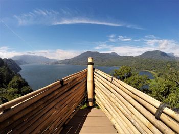 Wooden footbridge leading towards mountains against sky