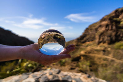 Midsection of person holding rock against sky