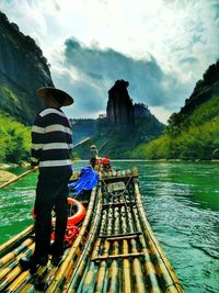 Man standing on wooden raft against rock cliffs and clouds