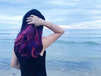Rear view of woman with dyed hair at beach against cloudy sky