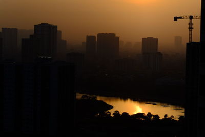 Silhouette buildings by lake against sky during sunset