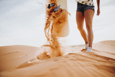 Cropped unrecognizable young female standing on sand with sand over her while preparing for sandboarding