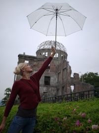 Smiling young woman holding umbrella against historic old ruin