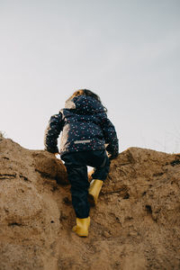 Rear view of girl climbing rock against sky