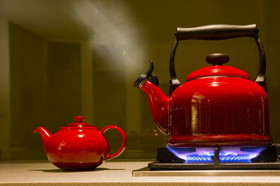 Steaming bright red kettle on gas stove with blue flames against a green wall in modern kitchen.