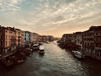 Boats moored in sea by buildings against sky during sunset