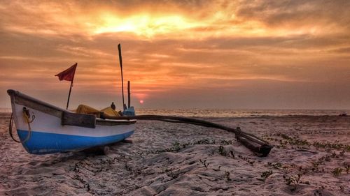 Boat moored on beach against sky during sunset