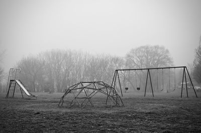Swing and slide at playground against sky during foggy weather