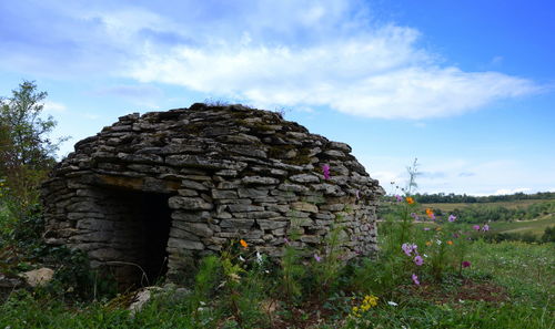 Stoned wall house on field against cloudy sky
