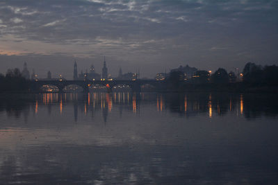 River by illuminated city against sky at sunset