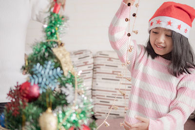 Cute girl with arms raised holding christmas decoration while standing against wall