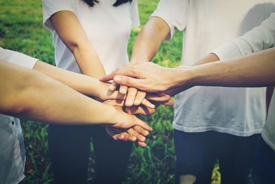 Midsection of friends stacking hands while standing at park