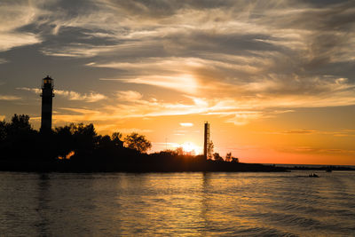 Silhouette lighthouse by sea against sky during sunset