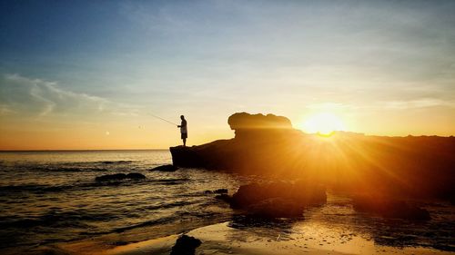 Silhouette rocks on beach against sky during sunset