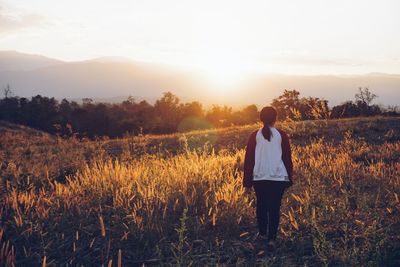 Rear view of woman standing on field against sky during sunset