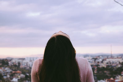 Rear view of woman looking up with cityscape in background against cloudy sky