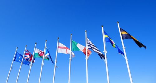 Low angle view of flags against clear blue sky