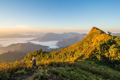 Rear view of woman standing on mountain against sky during foggy weather