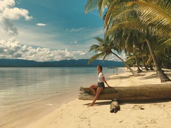 Woman sitting on tree trunk at beach