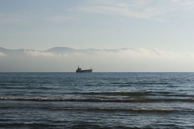 Distant view of boat sailing in sea against sky
