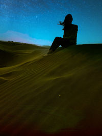 Silhouette man sitting on sand dune in desert