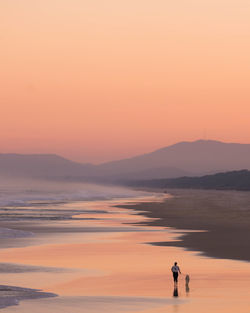 People standing on shore against orange sky