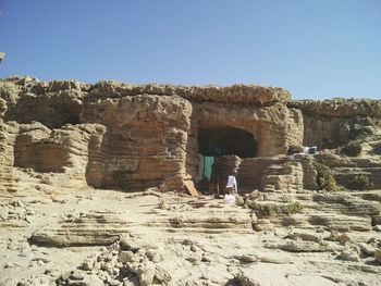 Rear view of man standing on rock formation against clear sky