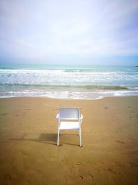 Empty chair on beach against sky