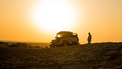 Side view of man walking towards vehicle on land against sky during sunset