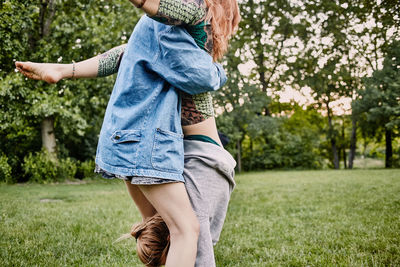 Midsection of woman assisting friend in doing handstand on field