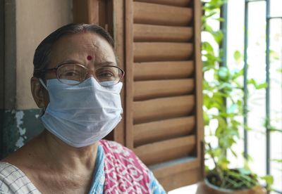 An aged indian woman wearing surgical face mask inside her home, during covid-19 pandemic