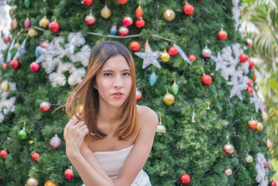 Portrait of young woman sitting against christmas tree