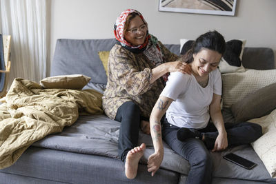 Happy mother massaging daughter with paraplegia sitting on sofa at home