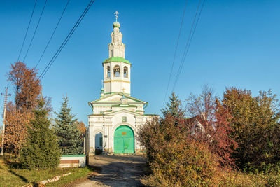 Street amidst trees and buildings against blue sky