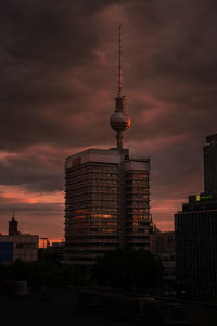 Communications tower in city against sky during sunset