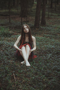 Portrait of young woman sitting on land in forest