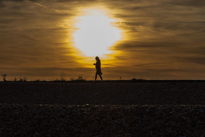 Silhouette woman walking on field against sky during sunset