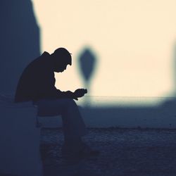 Side view of silhouette man using smart phone against sky