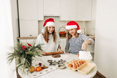 Two charming sisters in santa claus hats bake cookies for christmas in the kitchen