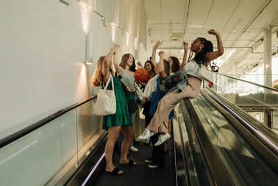 Teenage girls with hand raised enjoying on escalator in mall