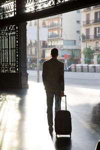 Rear view of man with luggage walking on floor