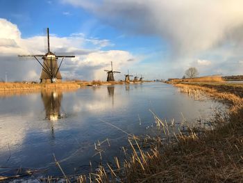 Panoramic view of traditional windmill by lake against sky