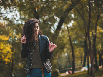 Young woman dancing to music against trees in park