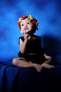 Cute girl wearing flowers while sitting against blue wall
