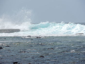 Waves splashing on shore against sky