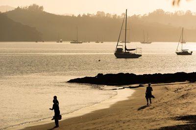 Silhouette people on beach against sky during sunset