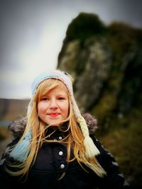 Portrait of smiling young woman wearing knit hat standing against rock formation