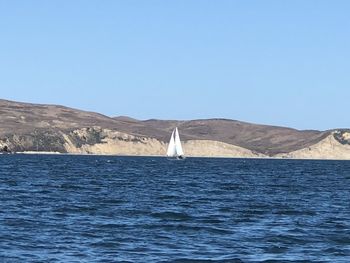 Sailboat in sea against clear blue sky