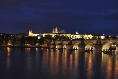 Illuminated buildings by river against sky at night